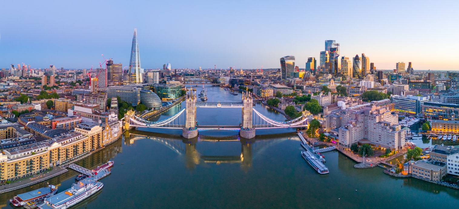 Luftaufnahme von London mit der beleuchteten Tower Bridge und der Skyline bei Sonnenuntergang.