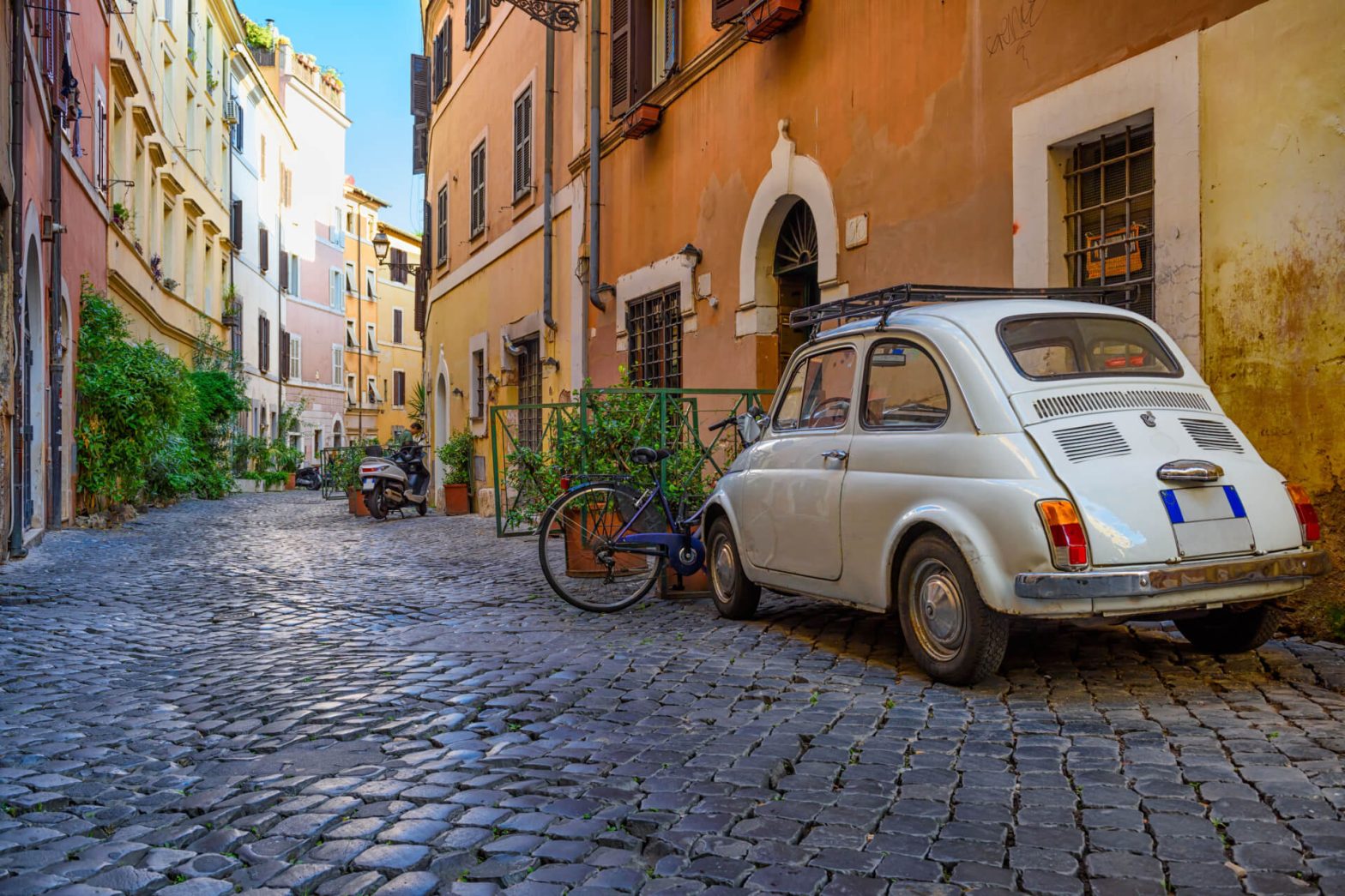 A classic white Fiat 500 parked on a cobblestone street in a quaint Italian neighbourhood, evoking the timeless charm of old-world Europe.
