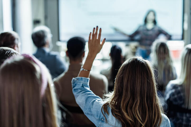 woman with blue shirt raising her hand at a training seminar