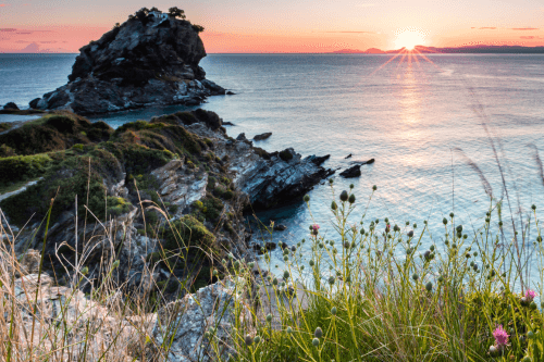 view to the sea on the island of scopelos with rocks and the sunset in pink and golden hues