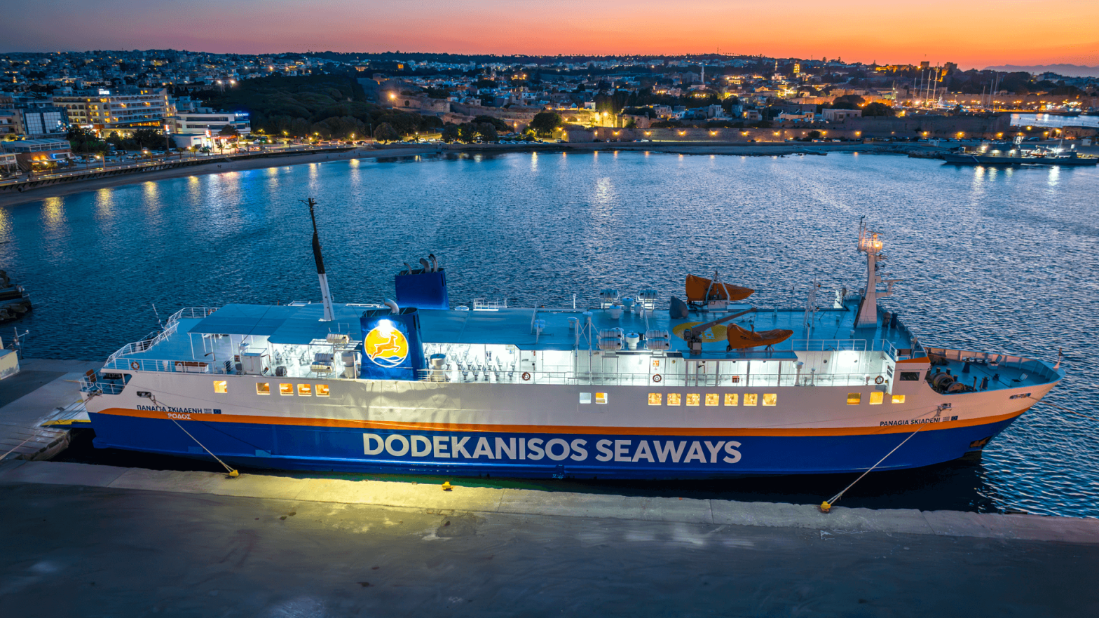 the ship Panagia Skiadeni docked in the harbour with blue and yellow colours while the sunset has created orange hues in the sky