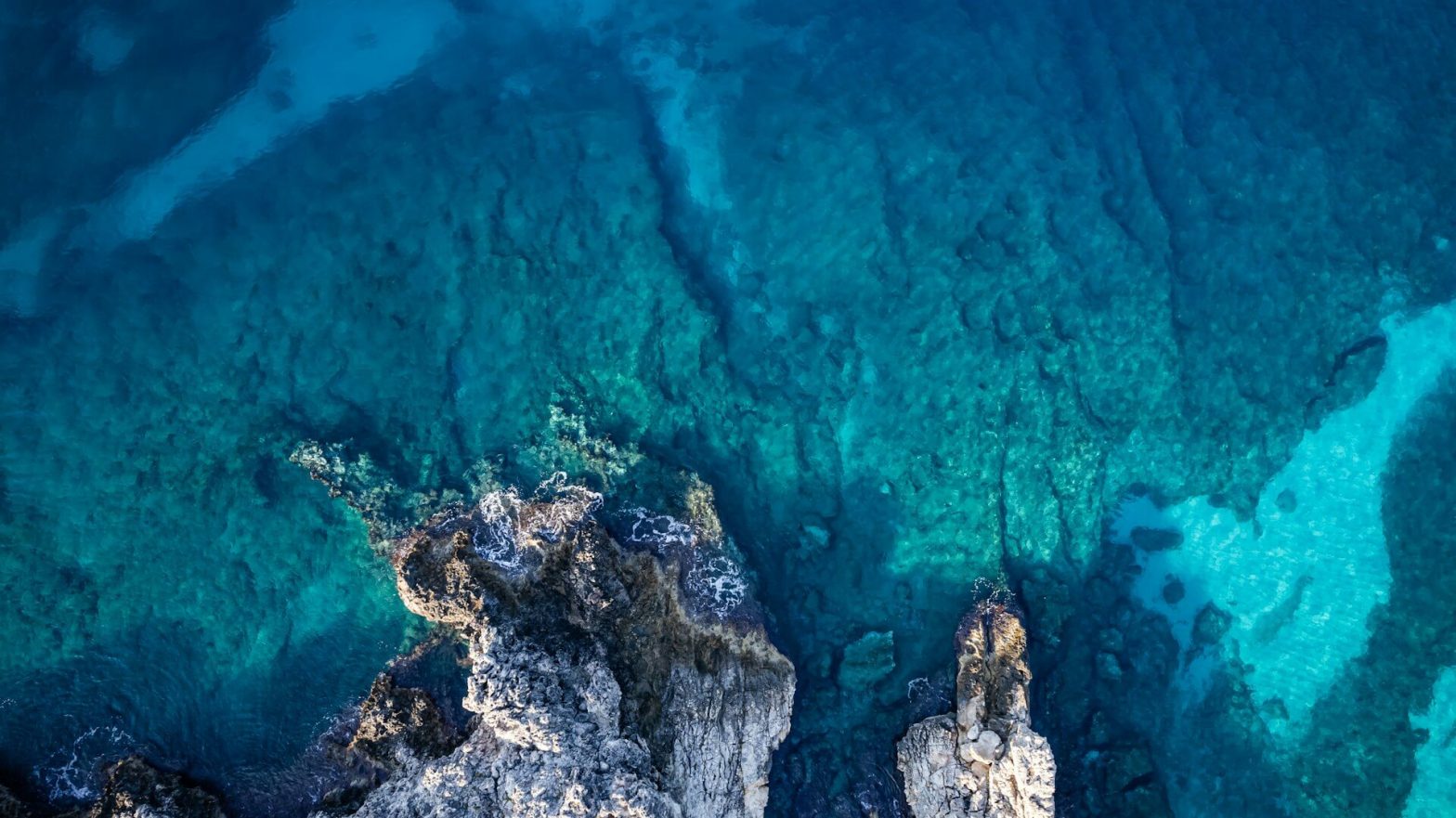 view of a bright blue sea and jagged rocks from above