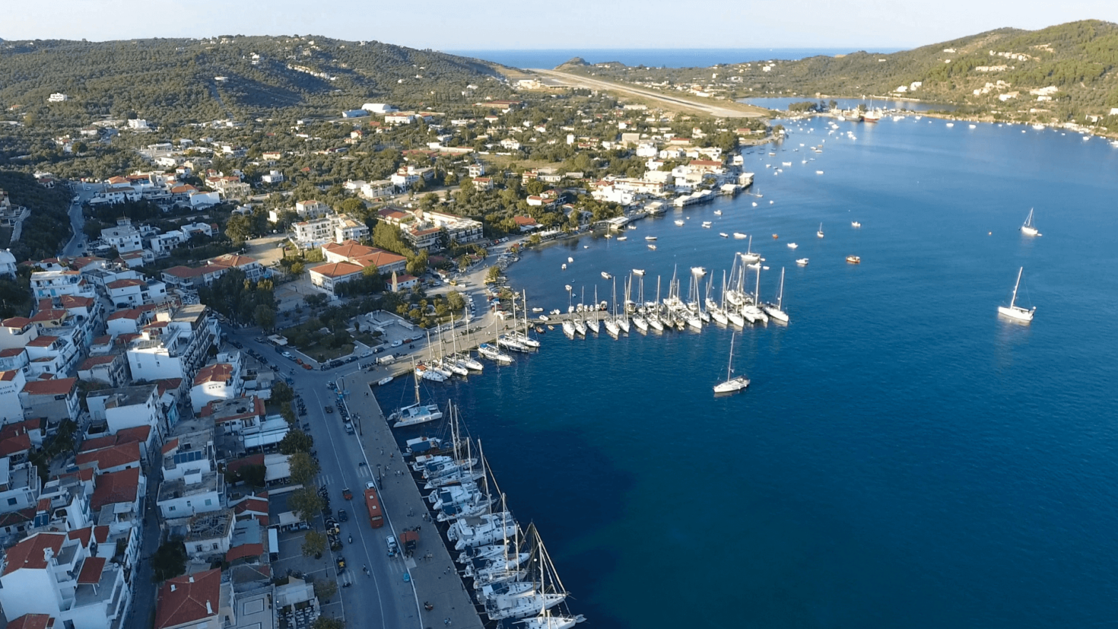 το λιμανι της Σκιαθου με πολλα καραβια και κτιρια με κοκκινες σκεπες αναμεσα στην πλουσια βλαστιση