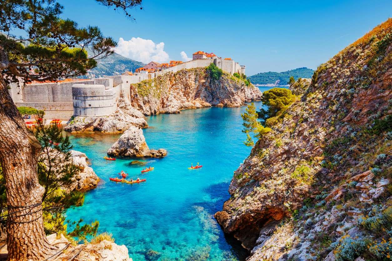 Scenic view of Dubrovnik, Croatia, with historic stone walls, turquoise waters, and kayakers.