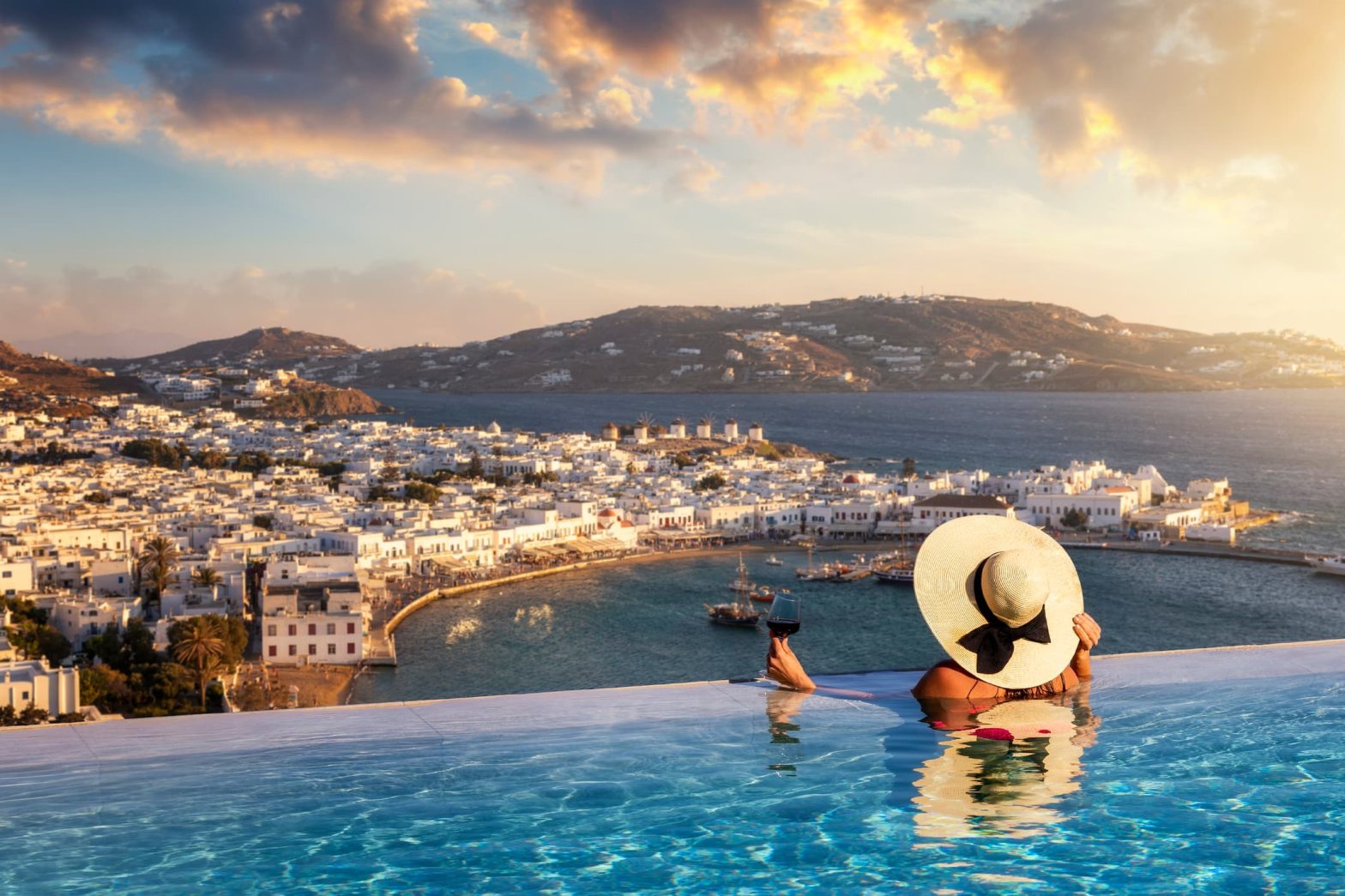 Una donna con un bicchiere di vino in piscina gode della vista sulla città dell'isola di Mykonos, in Grecia