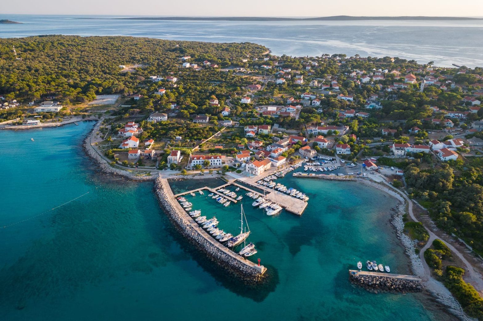 Pogled iz zraka na otok prekriven šumom i plavo more.