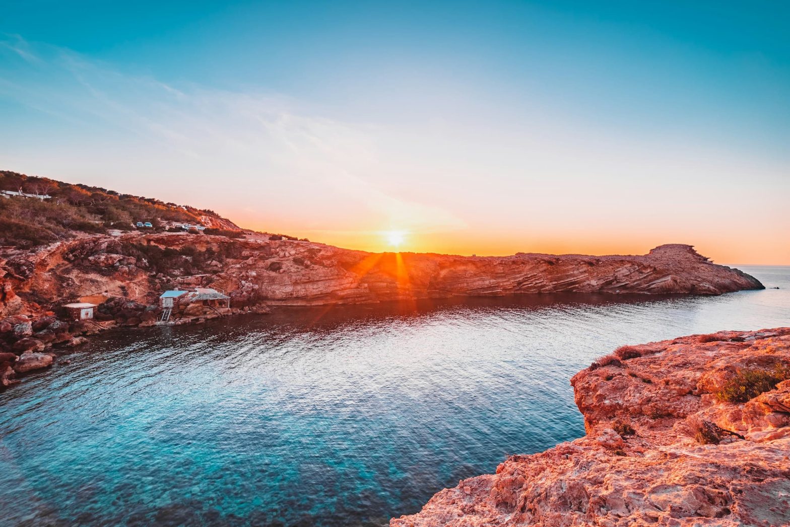 Tramonto su una cala rocciosa a Ibiza con acqua cristallina e cielo limpido