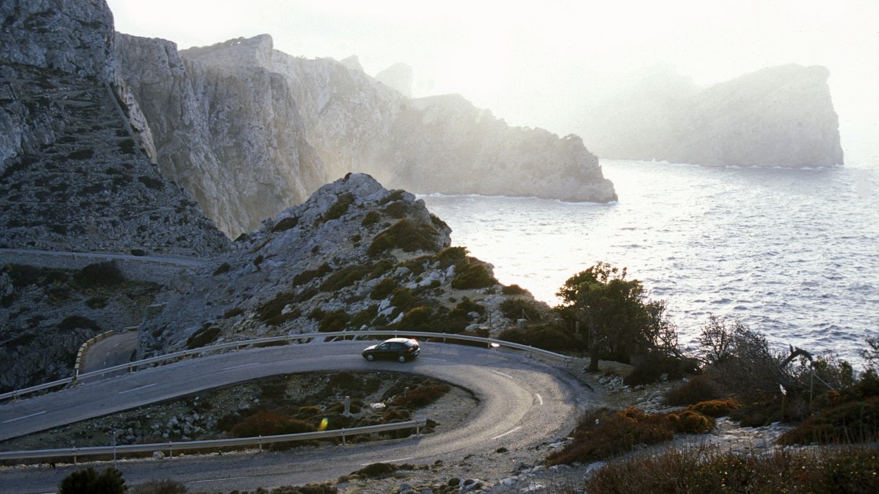 Cap de Formentor auf Mallorca bei Sonnenuntergang mit Auto in der Kurve.