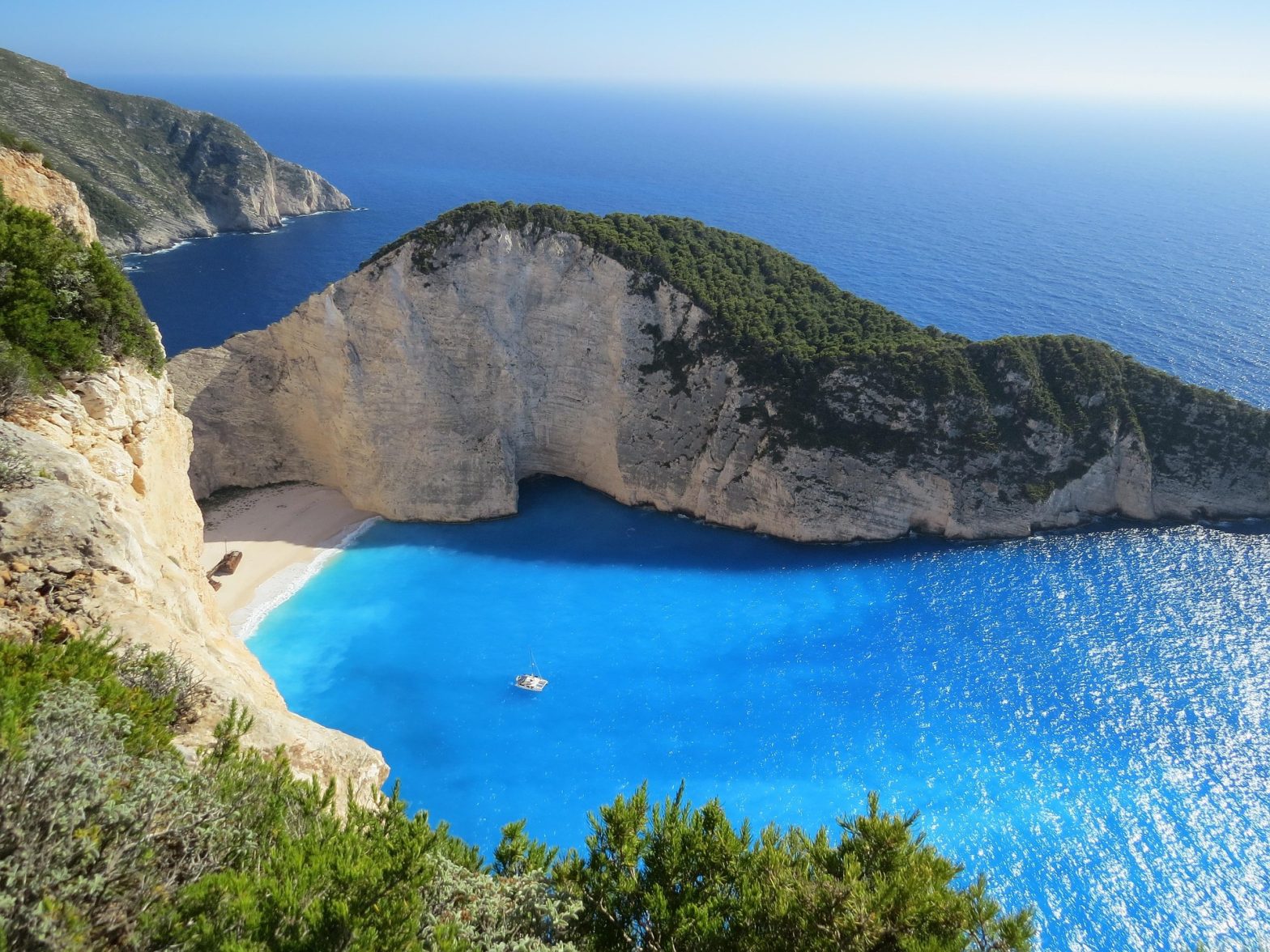 Spiaggia del relitto a Zante, Grecia, con sabbia chiara, mare turchese e alte scogliere ricoperte di vegetazione vista dall’alto.