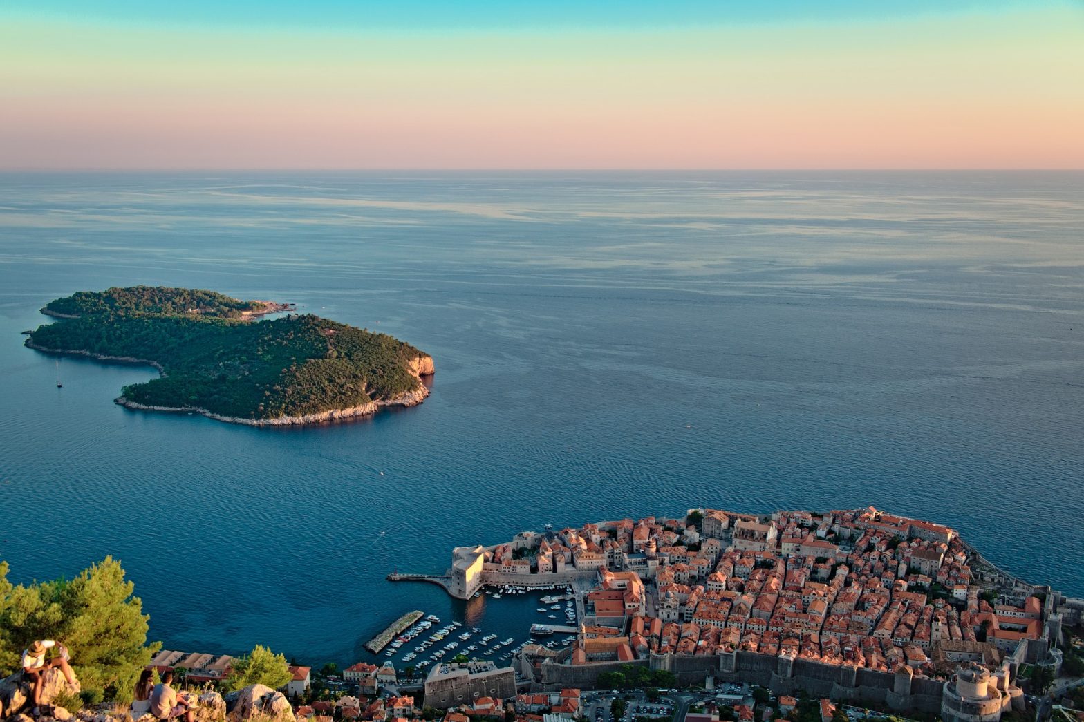 Vista panoramica su Dubrovnik e sull’isola di Lokrum al tramonto, con il centro storico e il porto circondati dal mare Adriatico.