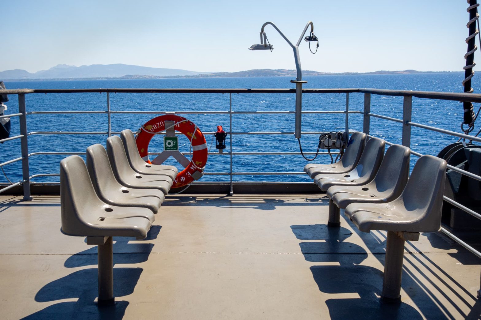 Outdoor seats on the deck of a ferry overlook the sea.