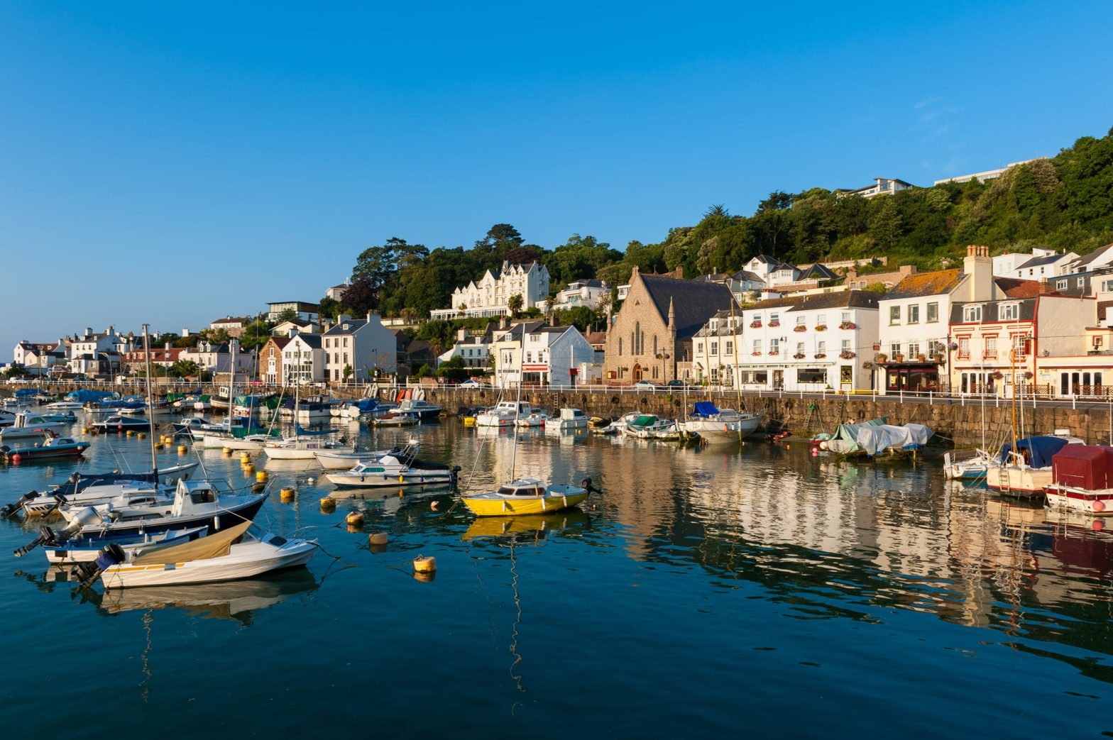 Un petit port de plaisance devant un front de mer typiquement anglais, sous un ciel bleu.