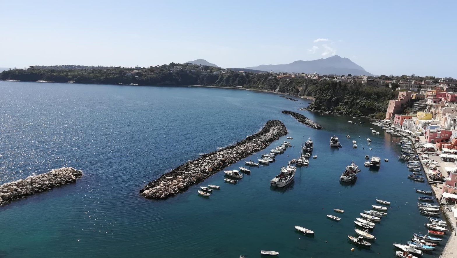 Veduta del porto di Procida con barche ormeggiate e case colorate affacciate sul mare.