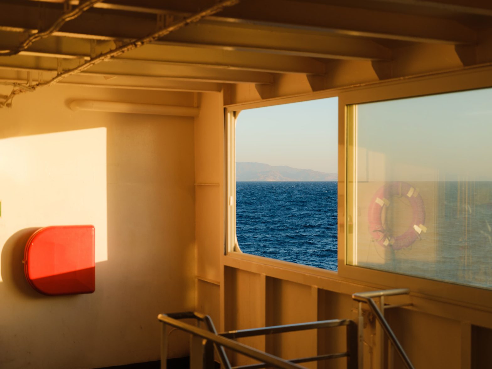 Vista del mare dal ponte interno di un traghetto, con luce del tramonto che entra dalle finestre durante la traversata.