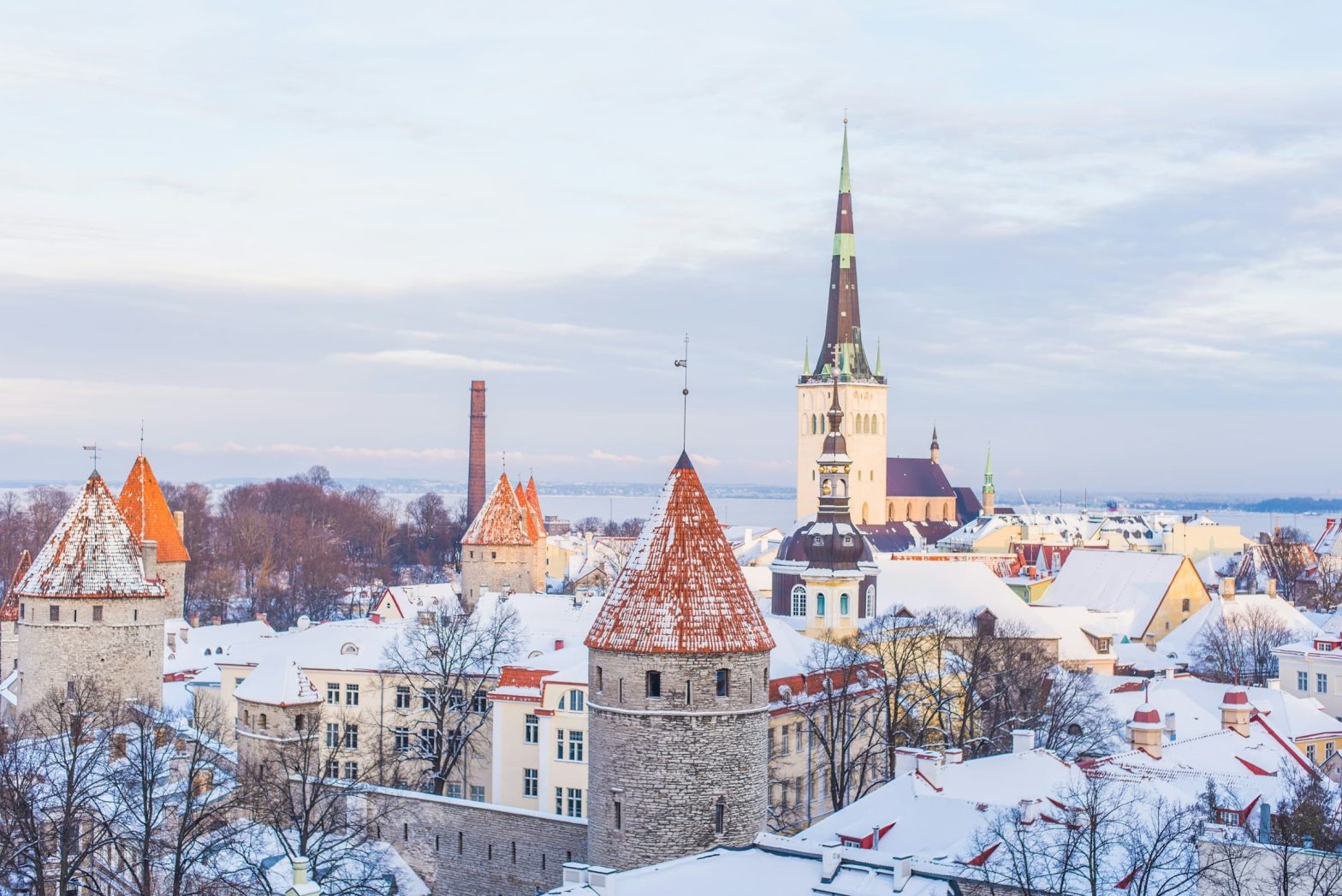 Vista panoramica di Tallinn innevata con le torri medievali e il campanile di St. Olaf illuminati dalla luce invernale.